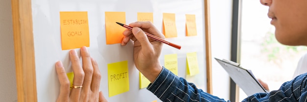 Business people arranging sticky notes commenting and brainstorming on work priorities colleague in a modern co-working space.