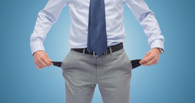 Фото Бизнес, люди, концепция банкротства и неудачи - крупный план бизнесмена, показывающего пустые карманы на синем фоне