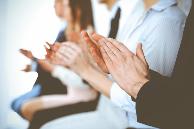 Business people clapping and applause at meeting or conference, close-up of hands. Group of unknown businessmen and women in modern white office. Success teamwork or corporate coaching concept.