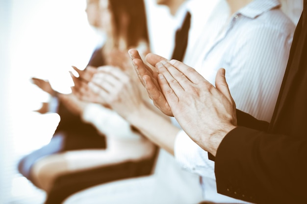 Business people clapping and applause at meeting or conference, close-up of hands. Group of unknown businessmen and women in modern white office. Success teamwork or corporate coaching concept.