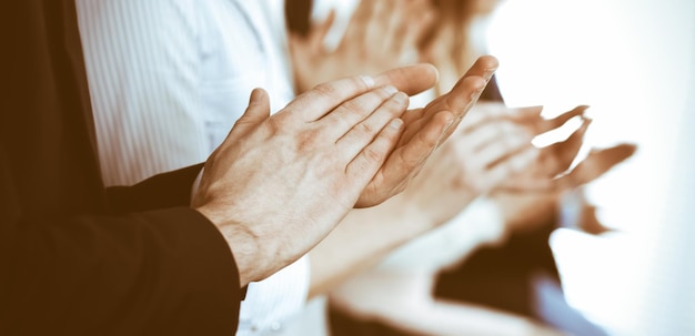 Business people clapping and applause at meeting or conference, close-up of hands. Group of unknown businessmen and women in modern white office. Success teamwork or corporate coaching concept.