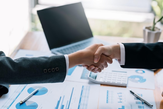 Business people collaboration deal shaking hands at meeting and financial paper graph on desk in modern office