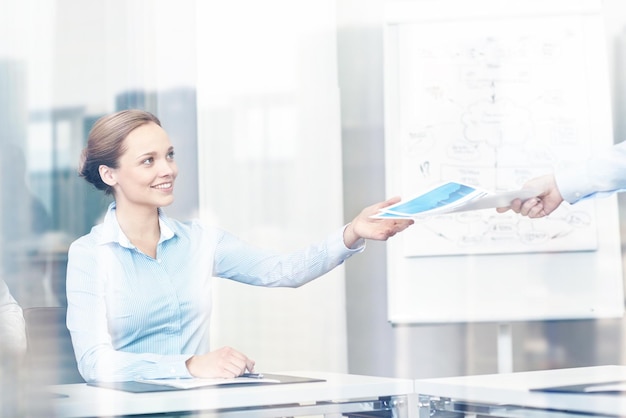 business and people concept - smiling businesswoman receiving papers from someone in office