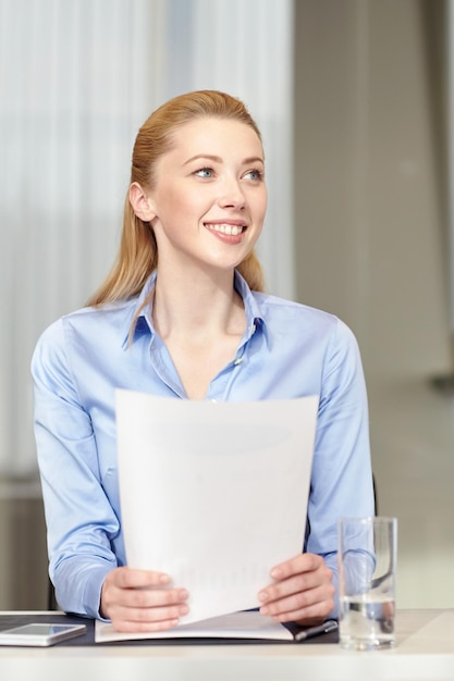 Business and people concept - smiling woman holding papers in office