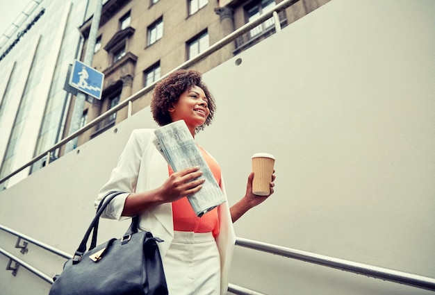 business and people concept - young smiling african american businesswoman with coffee cup going down stairs into city underpass