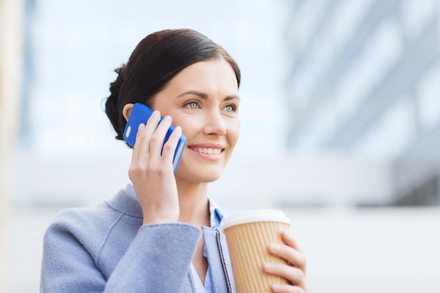 business and people concept - young smiling woman calling on smartphone and drinking coffee in city