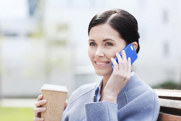 business and people concept - young smiling woman calling on smartphone and drinking coffee in city