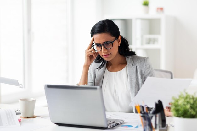 business, people, deadline and technology concept - stressed businesswoman with laptop computer and papers at office