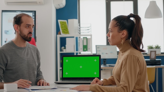 Business people doing teamwork on laptop with green screen at desk. Team of man and woman working with isolated mock up background and chroma key template on computer display.