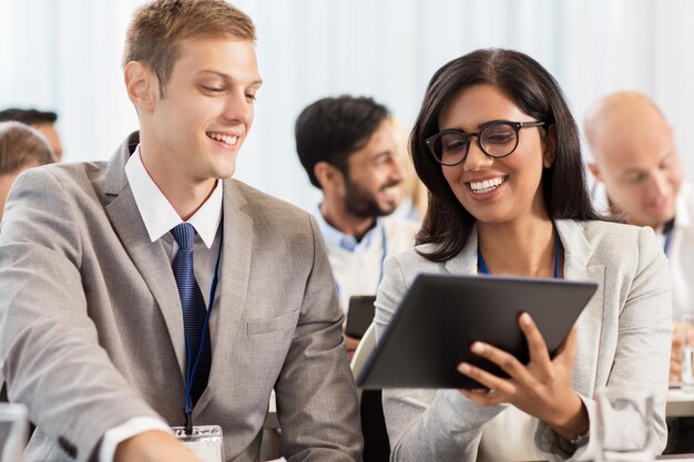 business, people and education concept - businessman and businesswoman with tablet pc computer at international conference