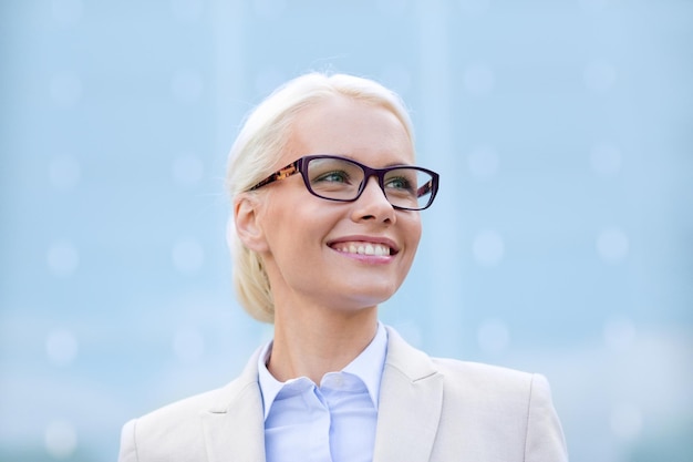 business, people and education concept - young smiling businesswoman over office building