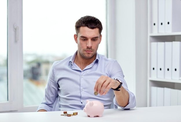 Photo business, people, finances and money saving concept - businessman with piggy bank and coins at office