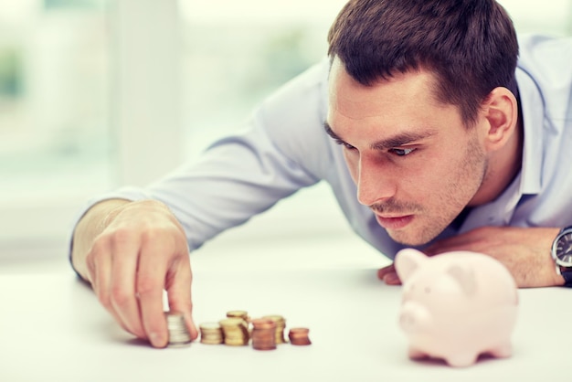 business, people, finances and money saving concept - businessman with piggy bank and coins at office