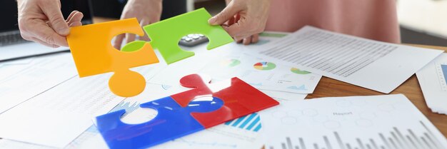 Business people folding colorful puzzle at table with documents closeup