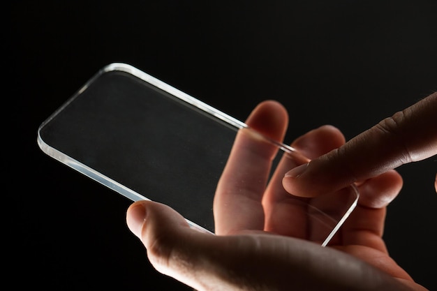 business, people and future technology concept - close up of businessman hands with transparent smartphone over black