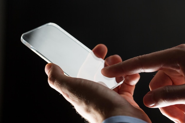 business, people and future technology concept - close up of businessman hands with transparent smartphone over black