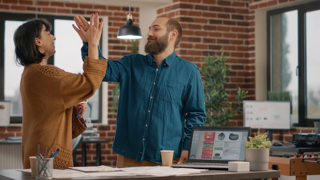 Business people giving highfive while working on successful project, feeling happy. Pleased man and woman doing teamwork and celebrating success after brainstorming ideas with files