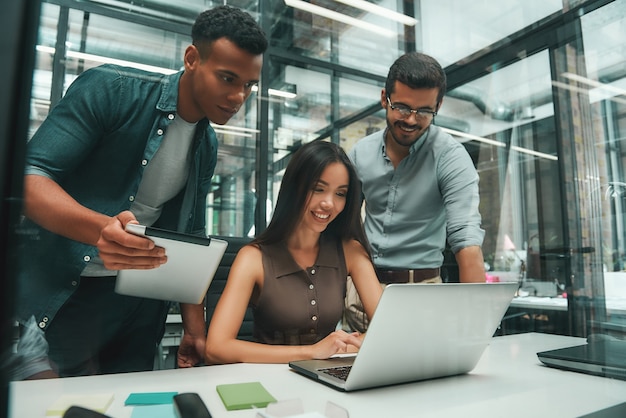 Business people group of three young and cheerful employees using modern technologies while working