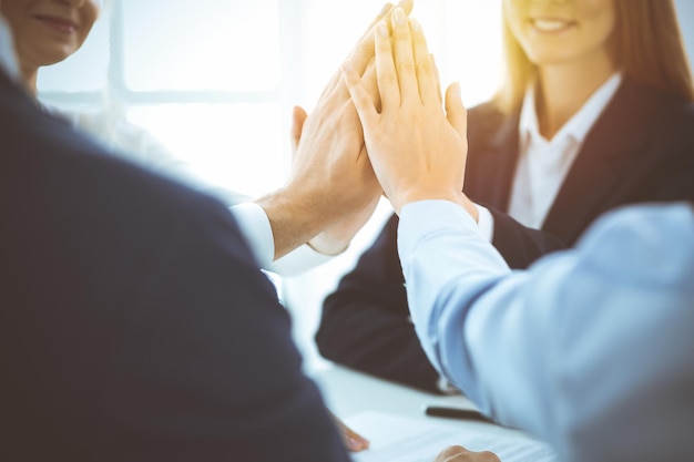 Business people happy showing teamwork and giving five showing unity and partnership in sunny office. Success and friendship concepts.