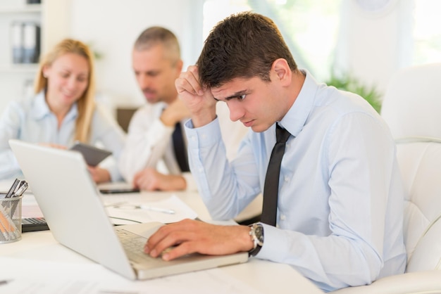 Business people having a meeting. Focus is on pensive young businessman who is worried looking at laptop. Selective focus.