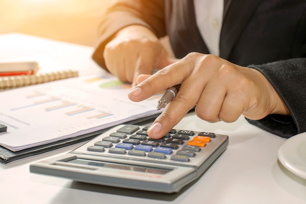 Business people hold pen to press calculator accounting ideas.