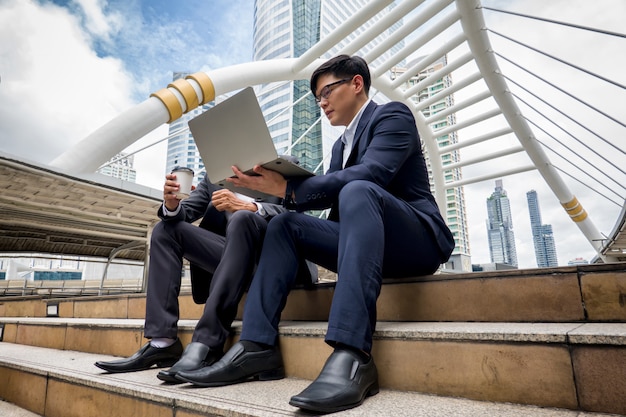 Photo business people holding laptop and discussing while sitting on step of  footbridge