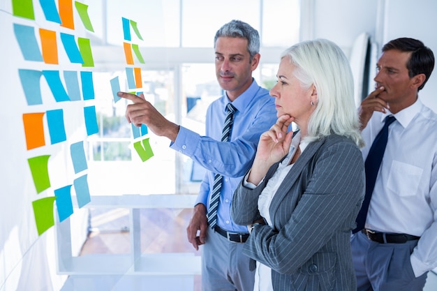 Business people looking at post it on the wall 