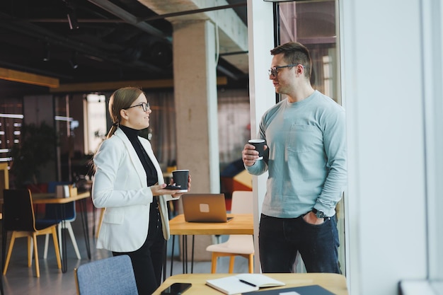 Business people man and woman over coffee discussing business looking at laptop modern workspace Colleagues work together in the office