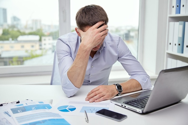 business, people, paperwork and deadline concept - stressed businessman with papers and charts sitting at table in office