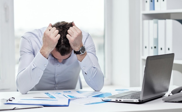 business, people, paperwork and deadline concept - stressed businessman with papers and charts sitting at table in office