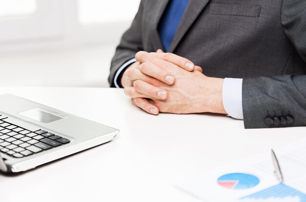 business, people, paperwork and technology concept - close up of businessman with laptop and papers in office