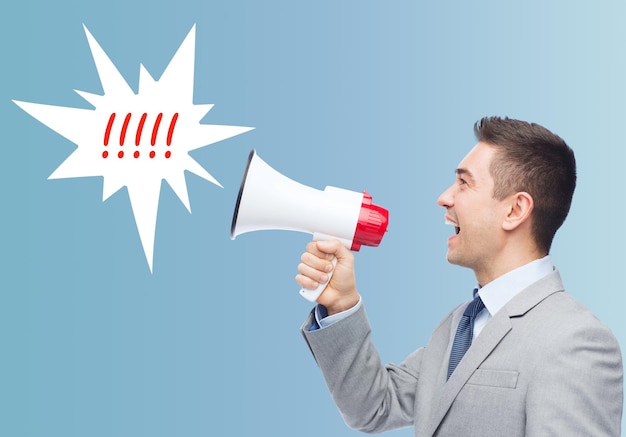 business, people and public announcement concept - happy businessman in suit speaking to megaphone over blue background