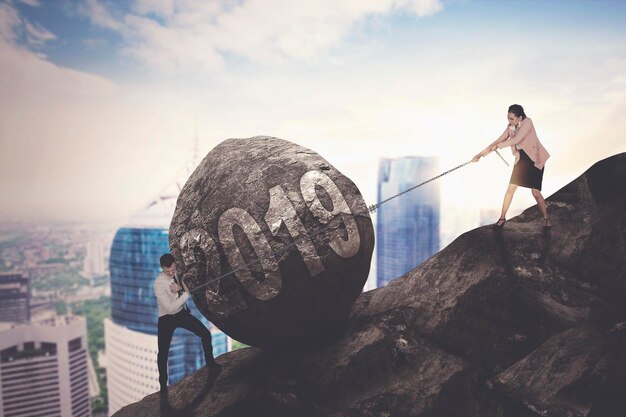 Business people pulling rock with 2019 text standing on hill against sky