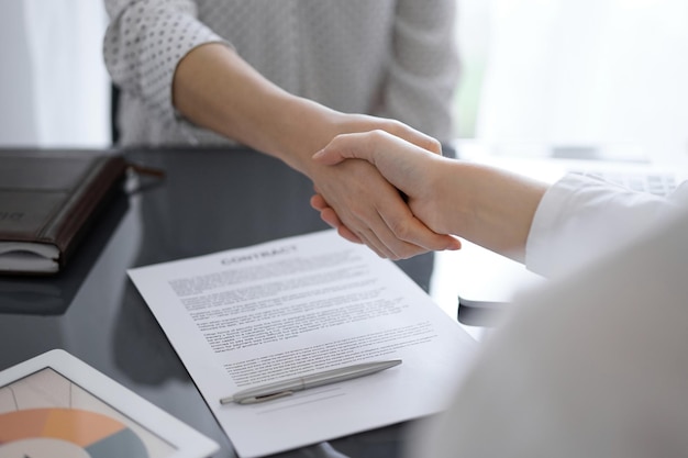 Business people shaking hands above contract papers just signed on the white table, closeup. Lawyers at meeting. Teamwork, partnership, success concept.