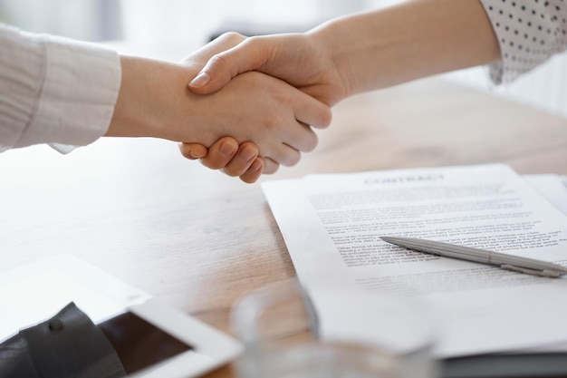 Business people shaking hands above contract papers just signed on the wooden table, close up. Lawyers at meeting. Teamwork, partnership, success concept.