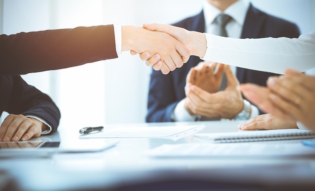 Business people shaking hands finishing up meeting or negotiation in sunny office. Business handshake and partnership concepts.