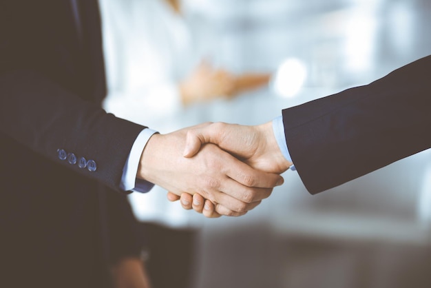 Business people shaking hands at meeting or negotiation, close-up. Group of unknown businessmen and a woman standing in a modern office. Teamwork, partnership and handshake concept.