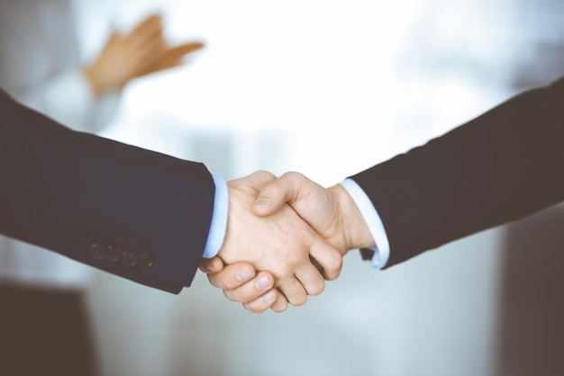 Business people shaking hands at meeting or negotiation, close-up. Group of unknown businessmen and a woman standing in a modern office. Teamwork, partnership and handshake concept.