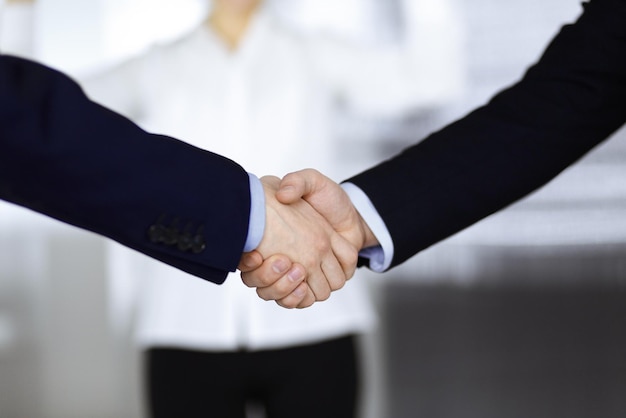 Business people shaking hands at meeting or negotiation, close-up. Group of unknown businessmen and a woman standing in a modern office. Teamwork, partnership and handshake concept.