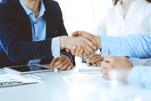 Business people shaking hands at meeting or negotiation, close-up. Group of unknown businessmen and women in modern office. Teamwork, partnership and handshake concept, toned picture