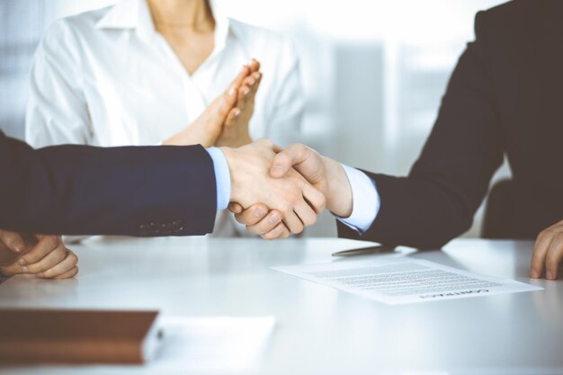 Foto uomini d'affari che stringono la mano alla riunione o alla negoziazione, primo piano. due uomini d'affari sconosciuti e una donna seduta alla scrivania in un ufficio moderno. concetto di lavoro di squadra, partnership e stretta di mano.