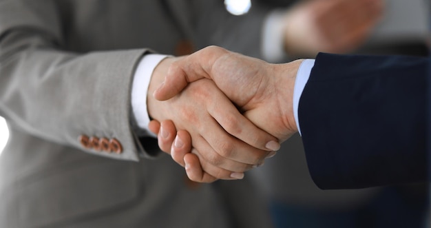 Business people shaking hands while standing with colleagues after meeting or negotiation, close-up. Group of unknown businessmen and women in modern office. Teamwork, partnership and handshake concep