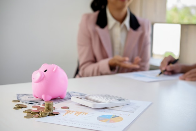 Business people sheltering coins and piggy bank at desk. 