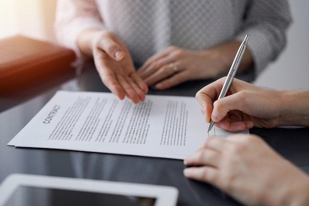 Business people signing contract papers while sitting at the glass table in office, closeup. Partners or lawyers working together at meeting. Teamwork, partnership, success concept