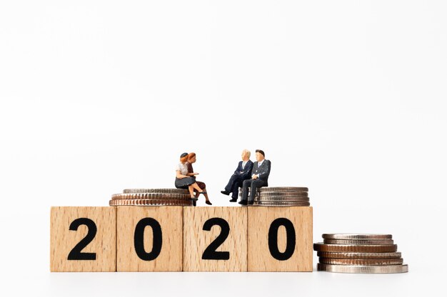 Business people sitting on wooden block number 2020 