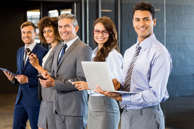 business people standing in a row and using mobile phone, lap top and digital tablet in office