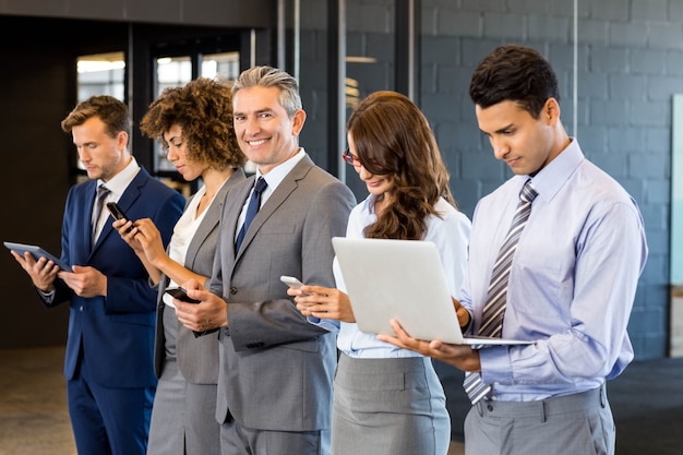 business people standing in a row and using mobile phone, lap top and digital tablet in office