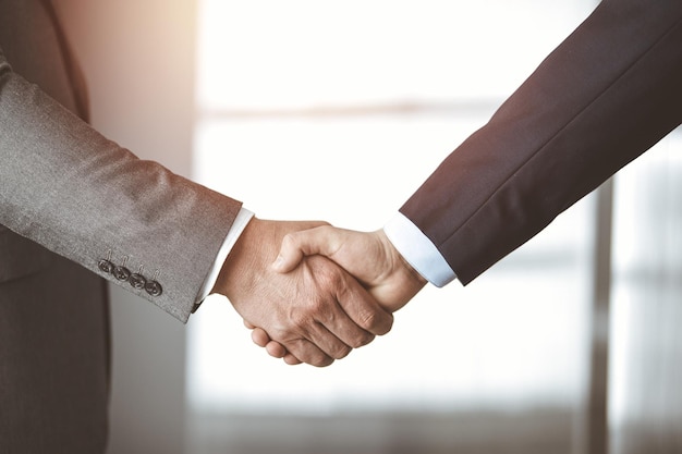 Business people standing and shaking hands in sunny office, close-up. Handshake and marketing.