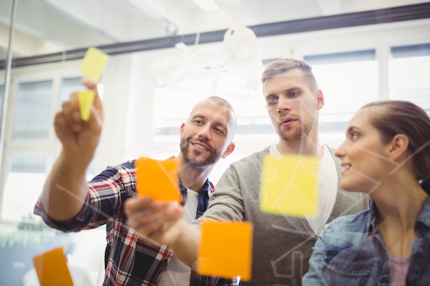 Business people sticking adhesive notes on window in office