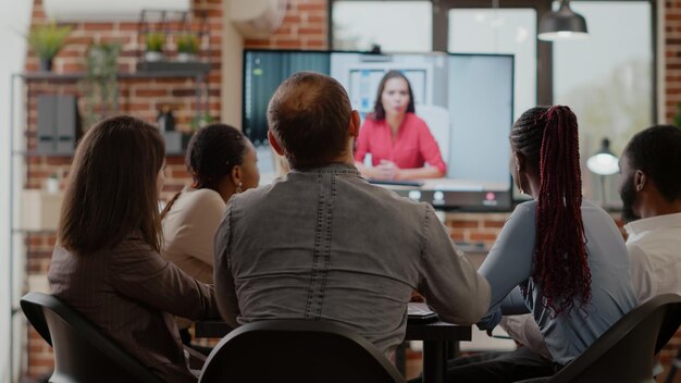 Business people talking on video call communication with woman,\
doing remote teleconference meeting in office. workmates using\
online video conference on internet connection for project\
briefing